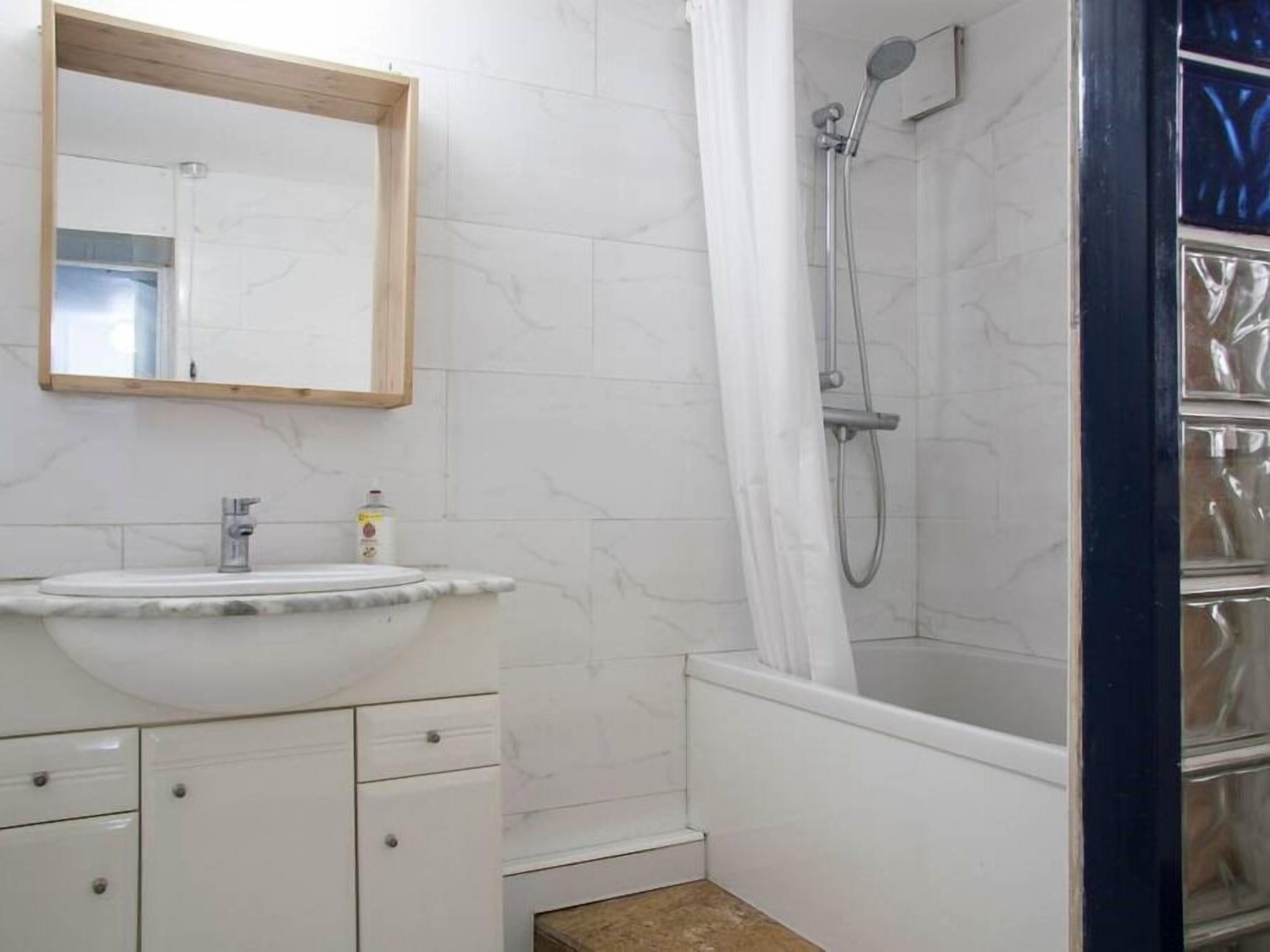 A bathroom with a marble sink, a shower, and a mirror.