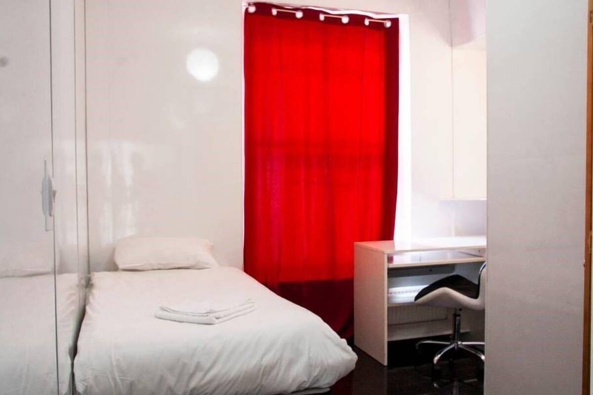 A small, modern bedroom with a bed, a desk, and a red curtain.