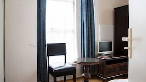 A room with a chair, a small round table, a television on a stand, and a cabinet. - Caledonian Studio Flats (London)