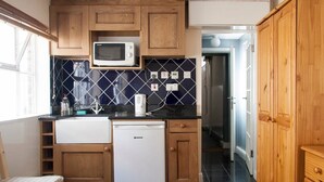 A compact kitchen with wooden cabinets, a microwave, a small refrigerator, and a tiled backsplash. - Caledonian Studio Flats (London)