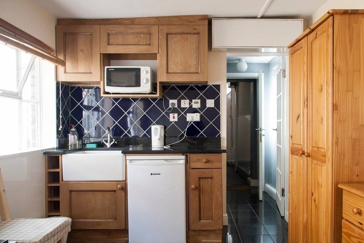 A compact kitchen with wooden cabinets, a microwave, a small refrigerator, and a tiled backsplash.