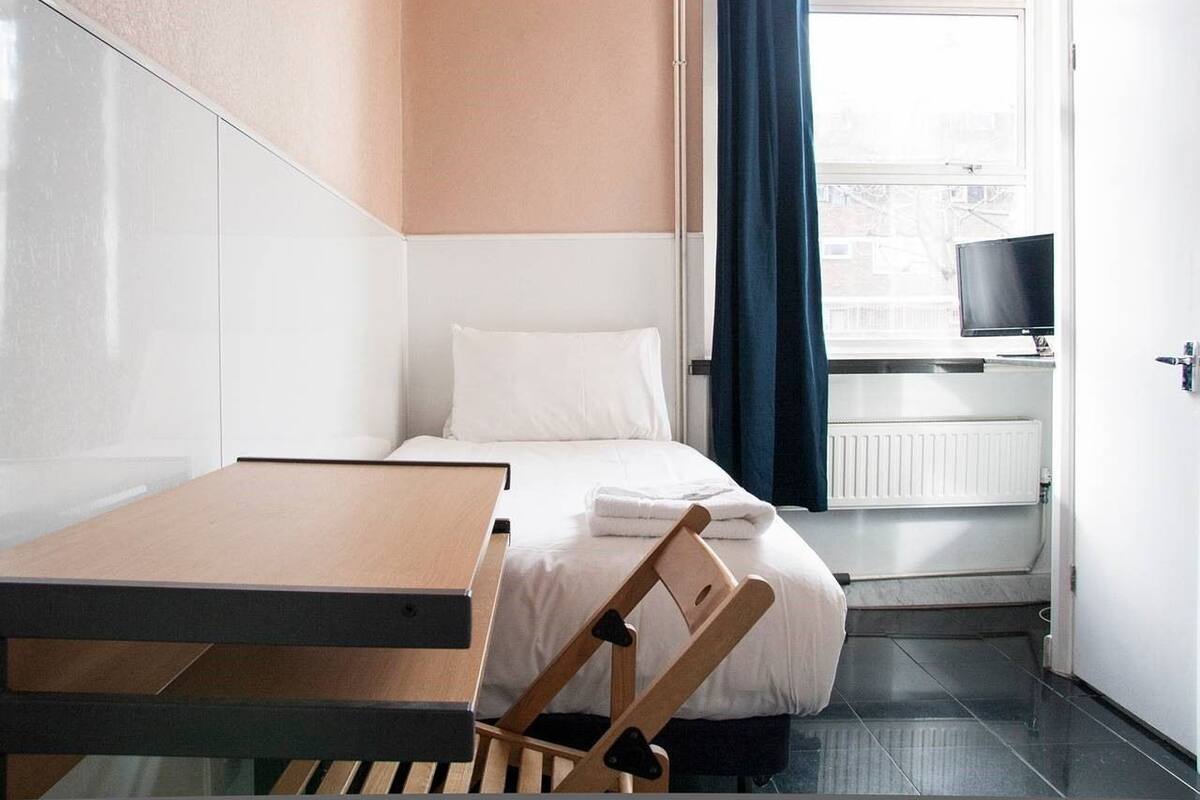 A hotel room with a bed, a desk, a chair, a TV, and a window with curtains.