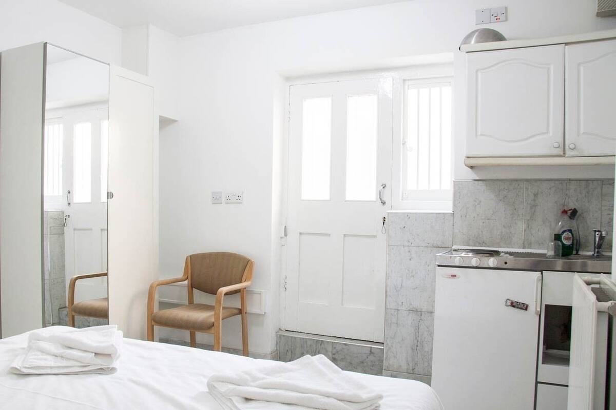 A hotel room with a bed, a chair, a small kitchenette, and a bathroom.