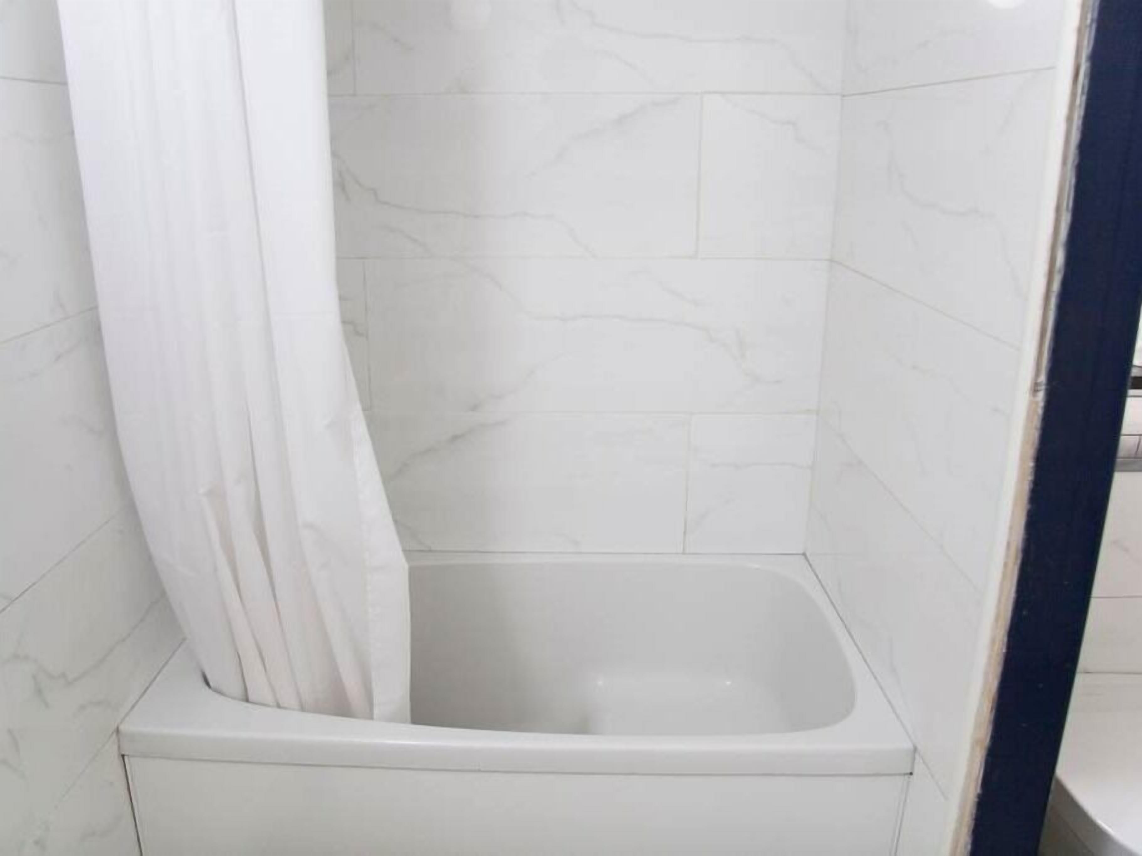 A bathroom with white marble tiles, a white bathtub, and a white shower curtain.