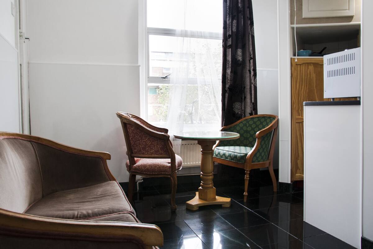 A small, modern living room with a sofa, two chairs, a small table, and a window with curtains.