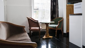 A small, modern living room with a sofa, two chairs, a small table, and a window with curtains. - Caledonian Studio Flats (London)