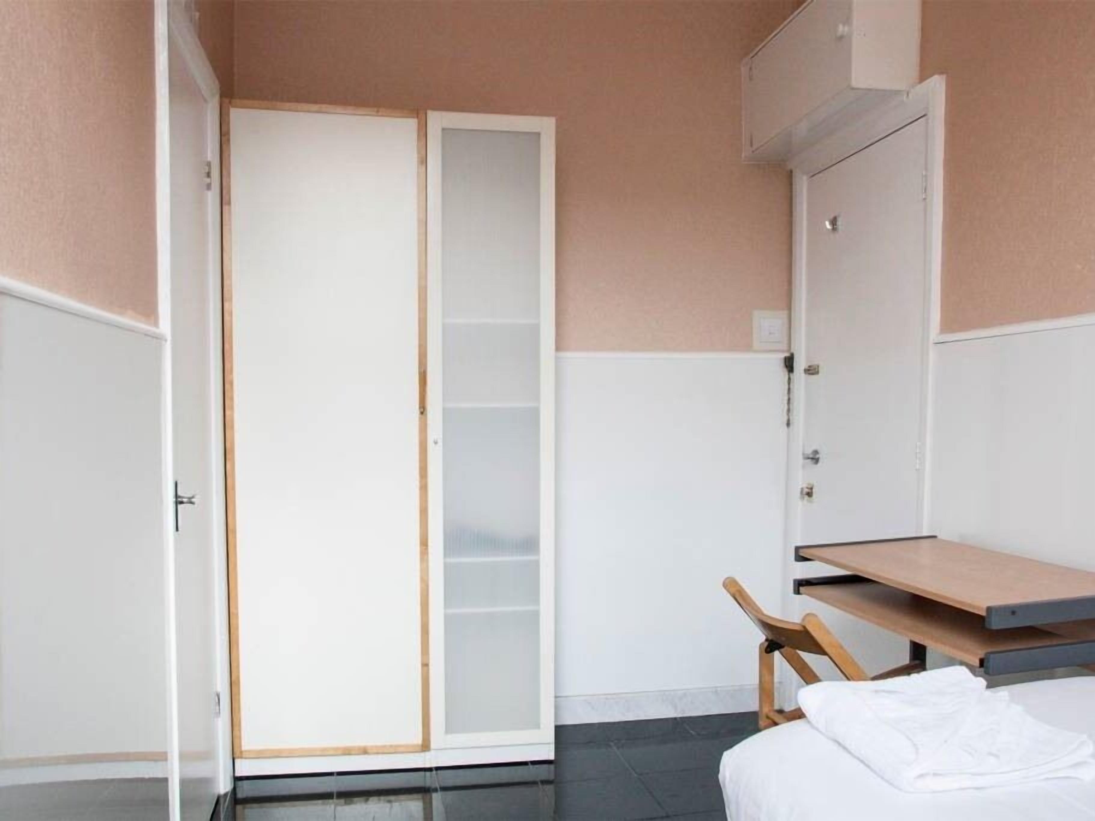A room with a bed, a wooden chair, a small table, and a wardrobe with a sliding door.