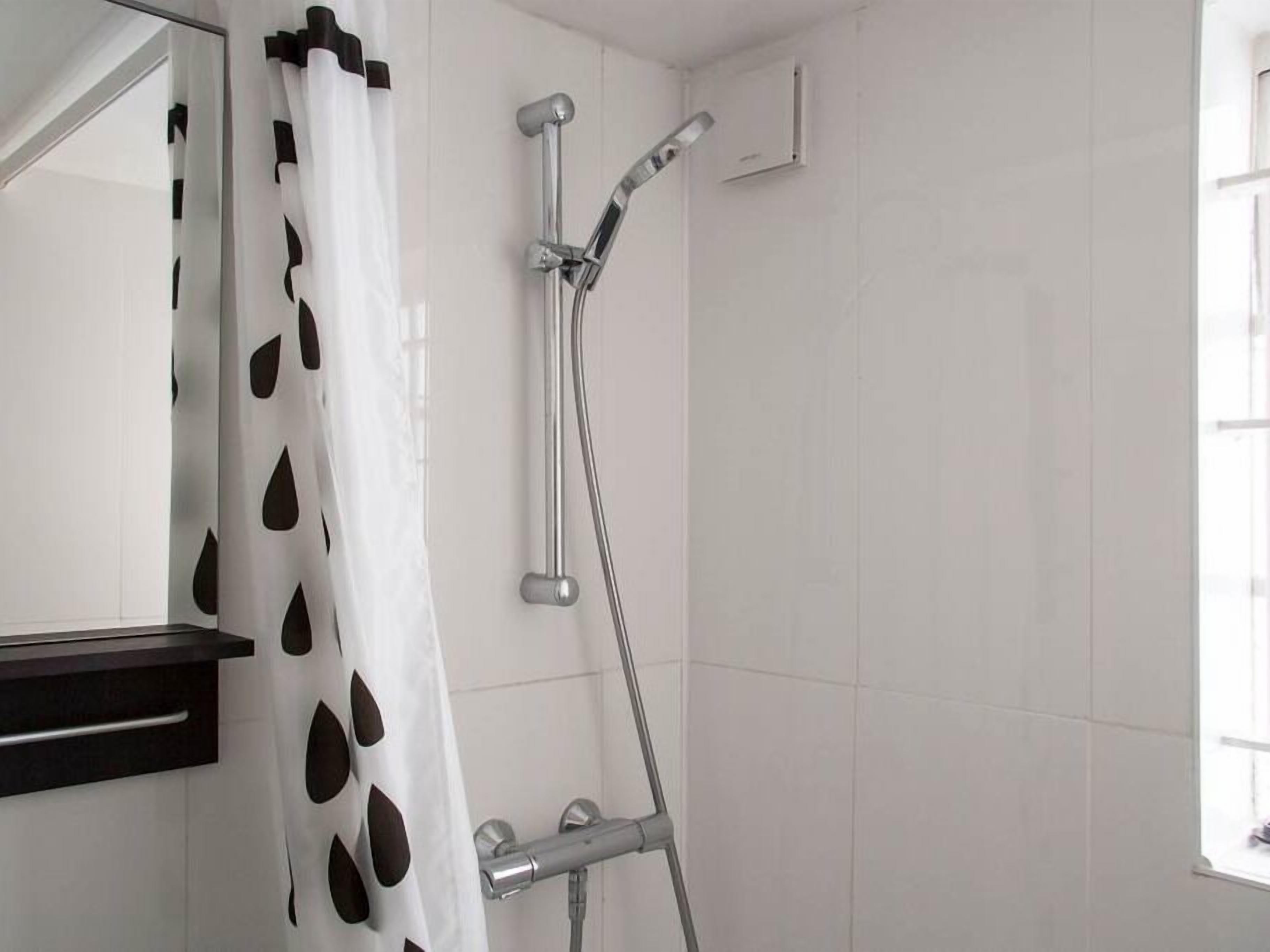 A bathroom with a shower, a mirror, and a window.