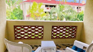 A balcony with white wicker furniture, a patterned floor, and a view of buildings with red roofs.
