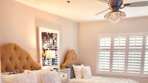 A bedroom with two beds, a ceiling fan, a window with blinds, and a framed picture on the wall.