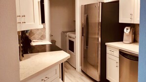 A modern kitchen with white cabinetry, a stainless steel refrigerator, a dishwasher, and a built-in oven.
