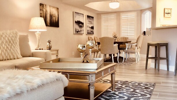 A living room with a sofa, coffee table, and a patterned rug. There is a dining area with chairs and a table in the background.
