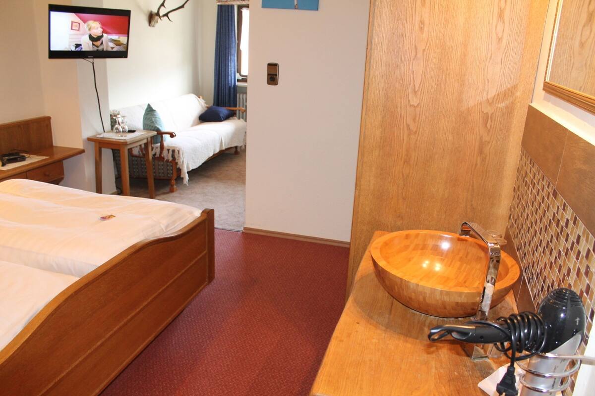 A bedroom with a wooden bed, a wooden bathroom vanity, and a television mounted on the wall.