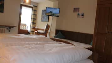 A hotel room with a large bed, a television mounted on the wall, a wooden headboard, and a window with curtains.