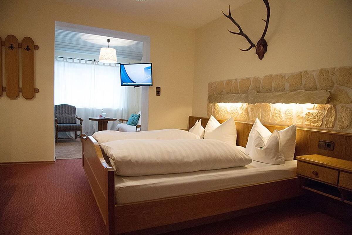 A hotel room with a large bed, a stone headboard, a mounted deer head, a television, and a small table with a chair.