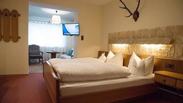 Una habitación de hotel con una cama grande, cabecera de piedra, cabeza de venado montada, un televisor y una pequeña mesa con una silla.
