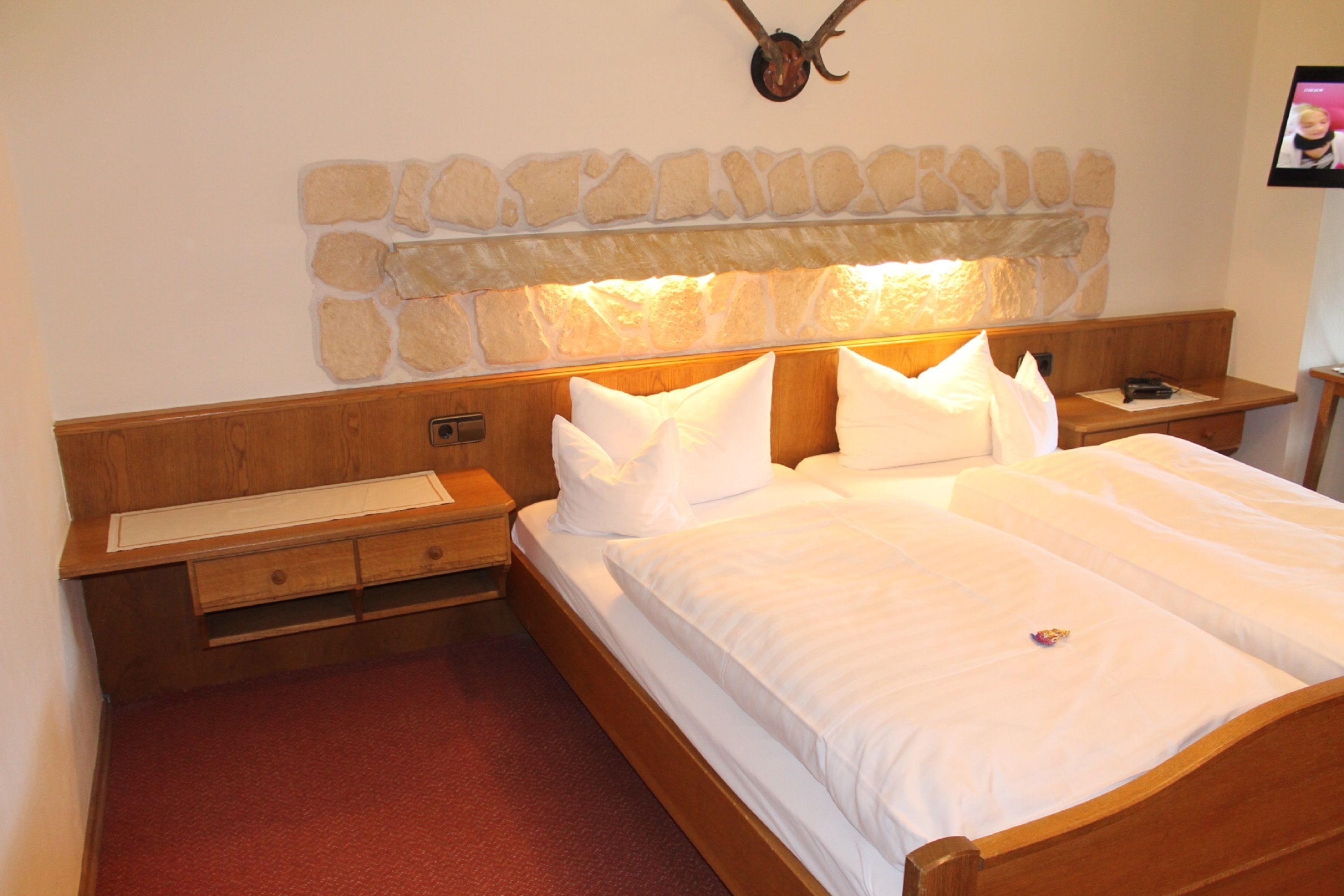 A bedroom with a stone headboard, wooden nightstands, a wooden bench, and a red carpet.