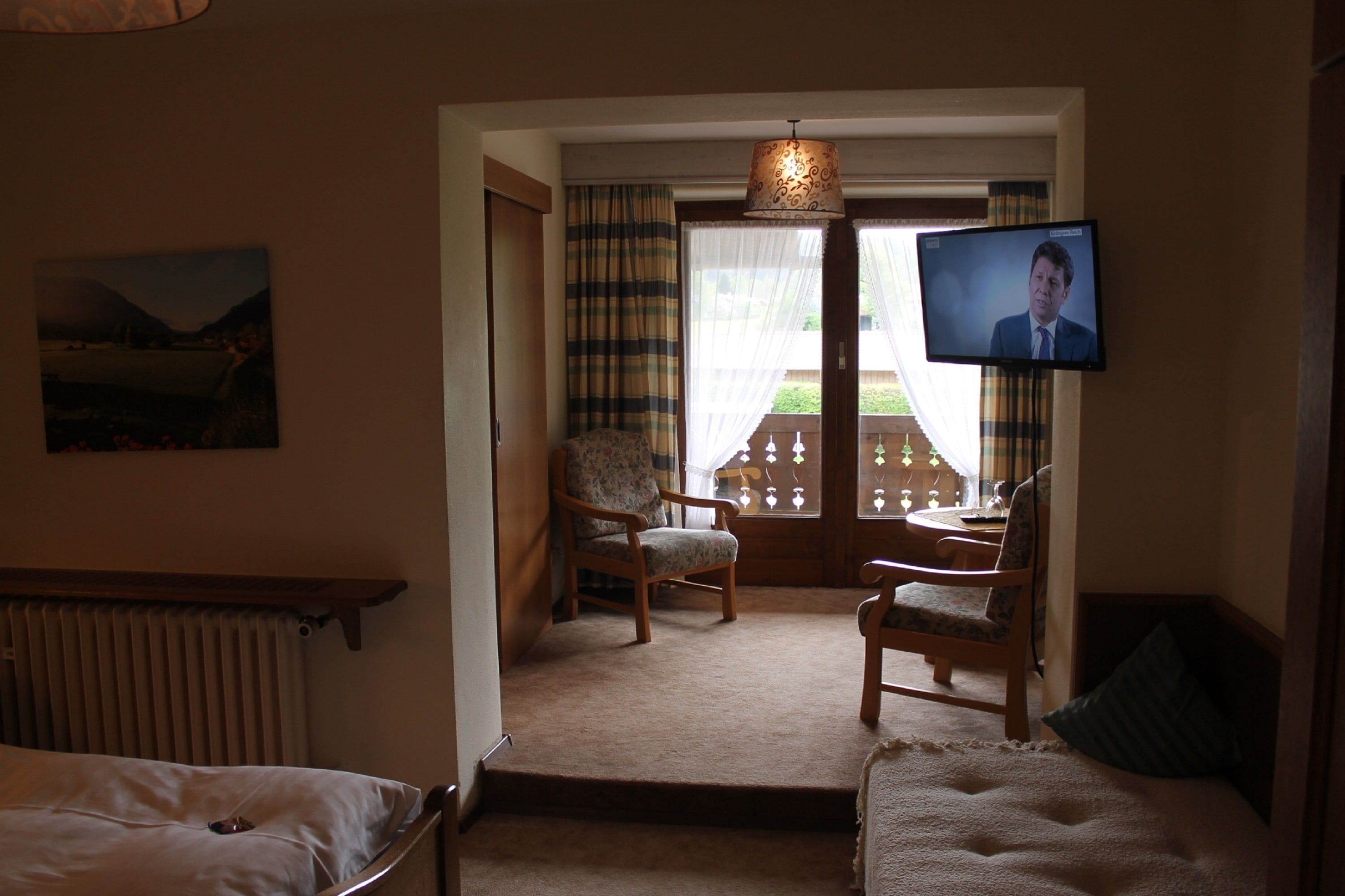 A hotel room with a bed, two chairs, a television, and a view of the outdoors.