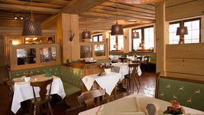 Un restaurante con vigas de madera, asientos tapizados en verde y mesas dispuestas con manteles blancos.