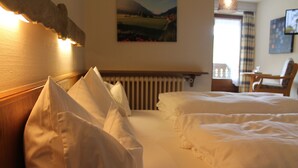 Habitación de hotel con dos camas, cabecero de madera, radiador, una silla y un cuadro en la pared.