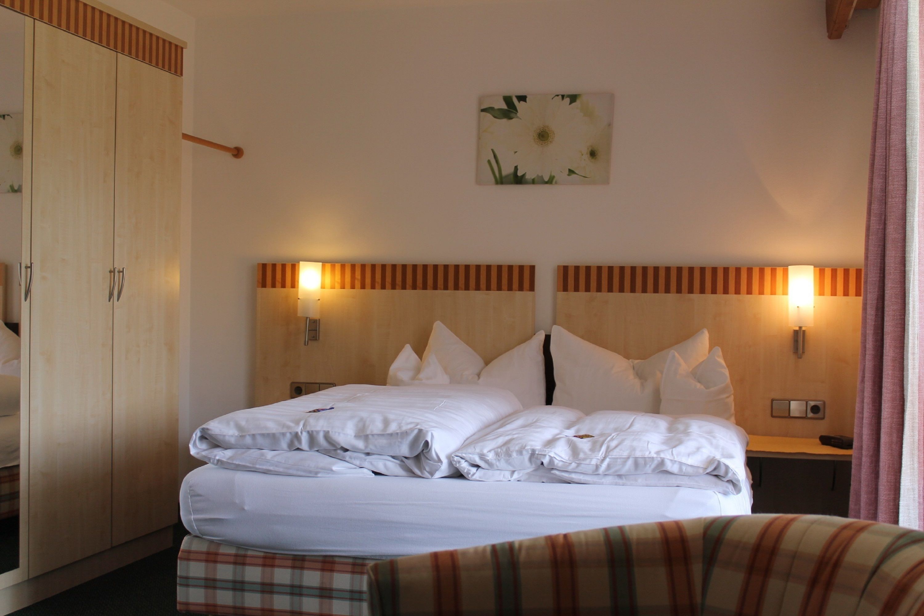 A hotel room with a bed, a wardrobe, a nightstand, and a wall-mounted lamp.
