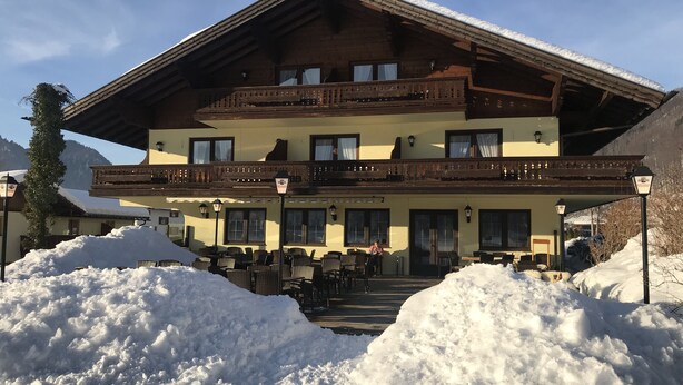 Un edificio de madera de dos pisos con balcones, un área de estar al aire libre cubierta y un paisaje cubierto de nieve.
