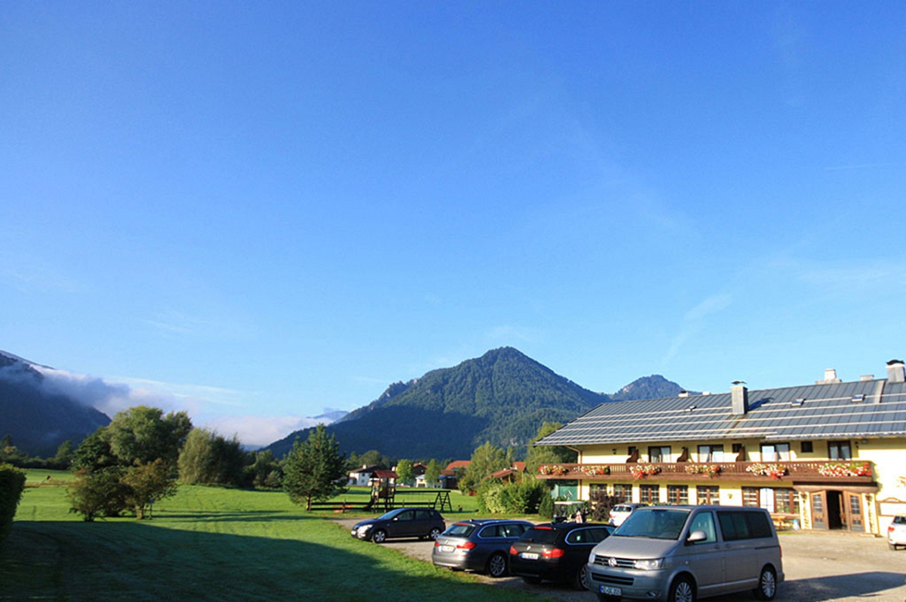 Un hotel con montañas al fondo, zona de estacionamiento y un edificio con balcón.