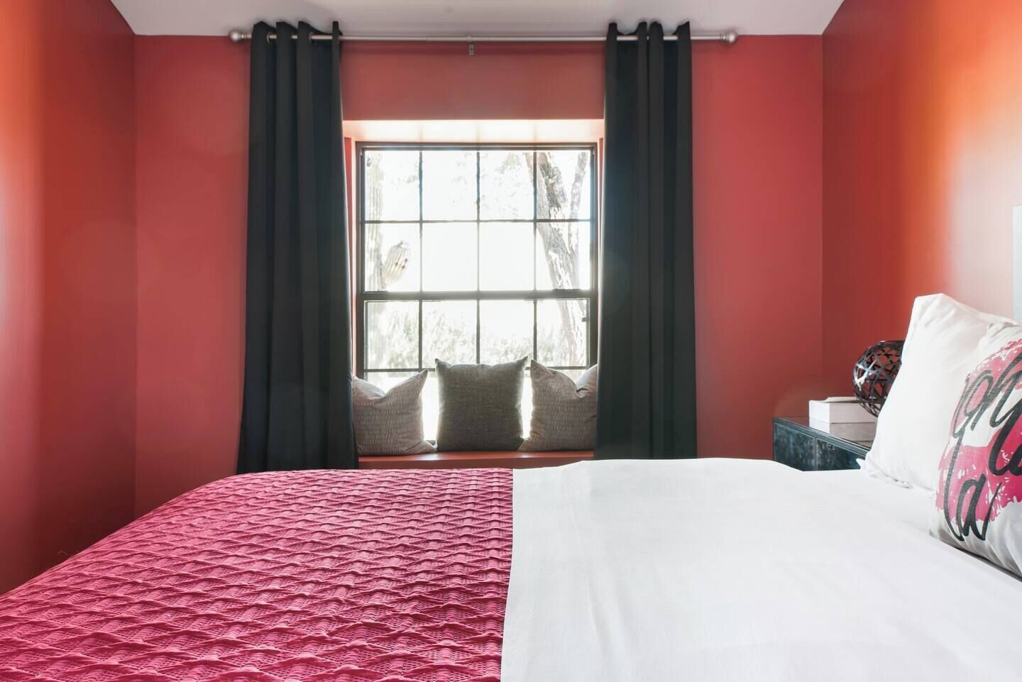A hotel room with a large bed, a window with curtains, and a view of trees outside.