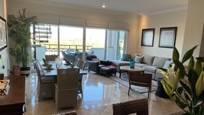 Uma sala de estar ampla com uma mesa de jantar, assentos confortáveis e janelas grandes com vista para o exterior.