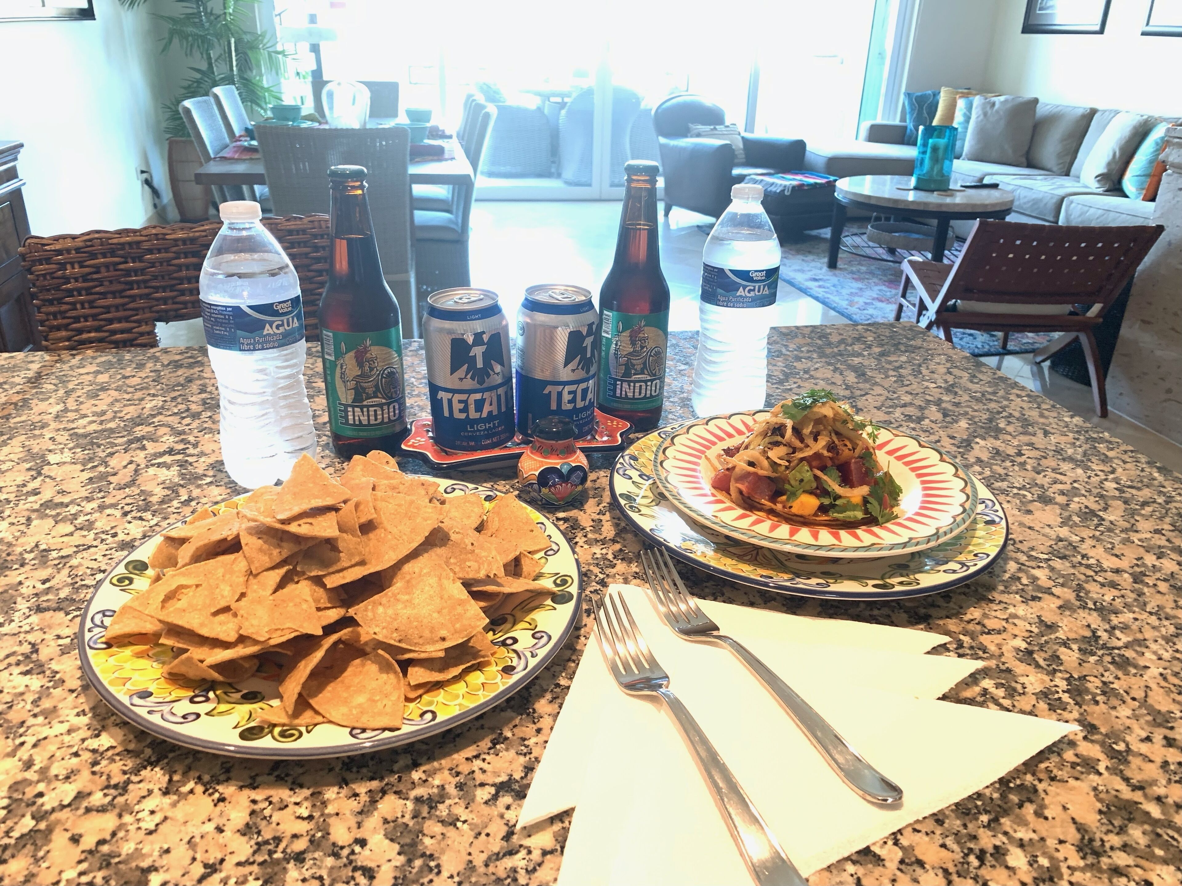 Une table à manger avec une assiette de nachos, une assiette de fajitas, ainsi que plusieurs bouteilles et canettes de boissons.
