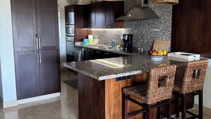 Uma cozinha moderna com armários de madeira escura, bancada de granito e uma ilha central com banquetas.