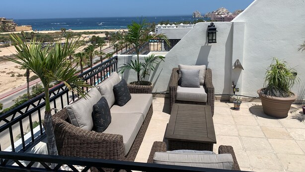Varanda com mobiliário de vime, plantas em vasos e vista para a praia e oceano.