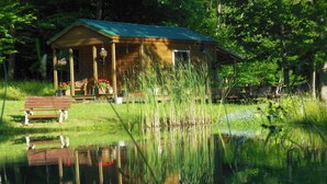 A wooden cabin with a porch, a bench, and a pond reflecting the structure.