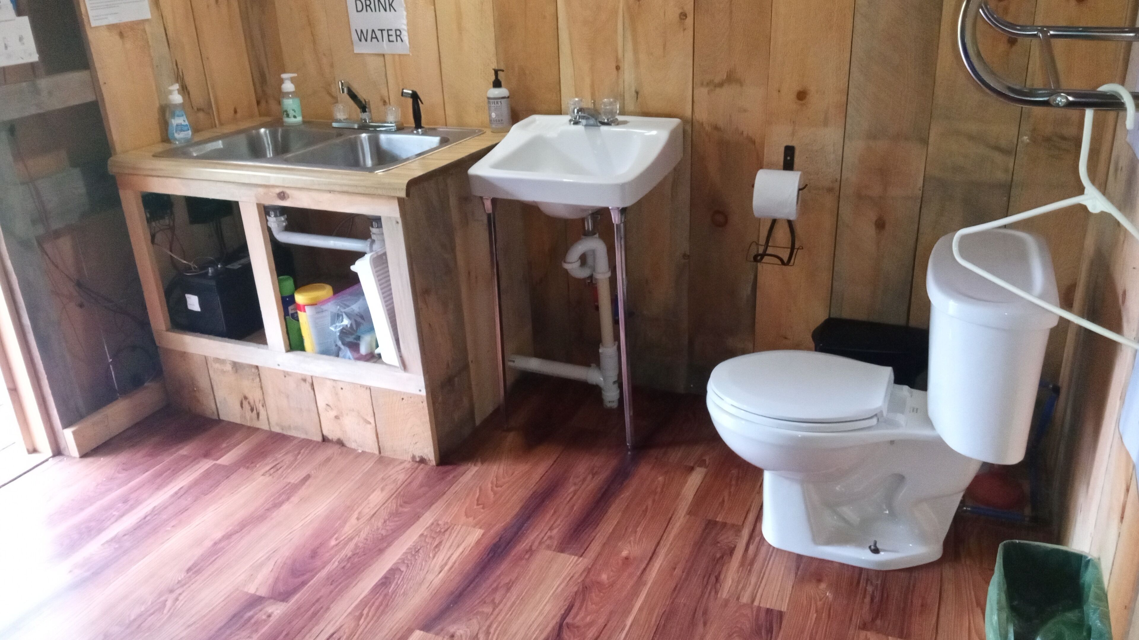 A compact bathroom with a wooden floor, a sink, a toilet, and a small cabinet with cleaning supplies.