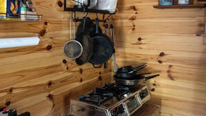Une cuisine compacte aux murs en bois, avec un poêle, des casseroles suspendues et un petit réfrigérateur.