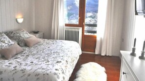 Une chambre à coucher avec un lit, une table de chevet, une commode et une vue sur les montagnes par la fenêtre.