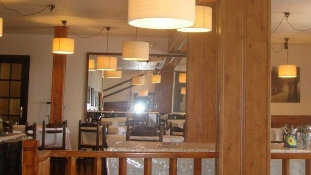 L’intérieur d’un restaurant est aménagé avec des meubles en bois, des luminaires suspendus et un bar où l’on peut voir des verres et des bouteilles.