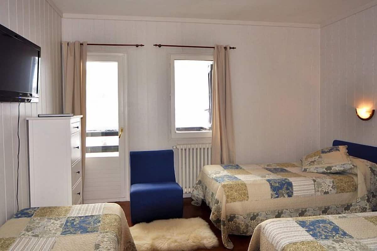 Une chambre avec deux lits, un bureau, une chaise, une télévision et des fenêtres avec des rideaux.