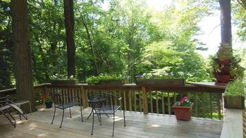 Una terrazza in legno con sedie e fioriere in metallo, circondata da alberi.