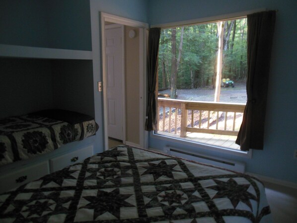 A bedroom with a bed, a door, and a window with a view of trees and a deck. - Serenity Cabin:Authentic Rustic Forest Retreat/Mountain View
Hiking/Pet friendly (Wellsville)