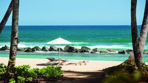 A beach with a white umbrella, lounge chairs, and a view of the ocean. - Dorado Beach a Ritz Carlton Reserve (Dorado)