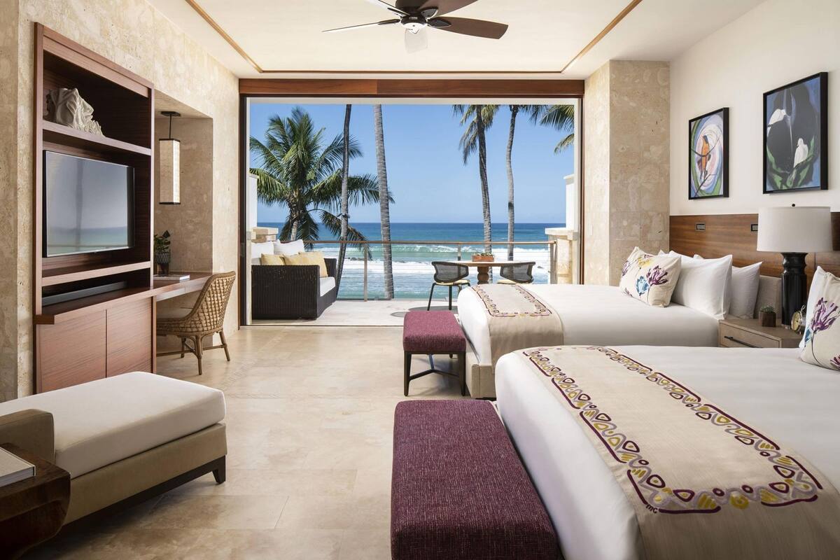 Habitación de hotel con balcón, televisión, cama, escritorio y una silla.