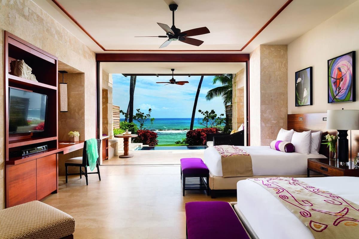 Habitación de hotel con televisión, cama, escritorio, silla y vista al océano.