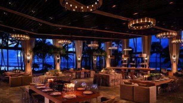 A spacious dining area with multiple tables, elegant chandeliers, and large windows offering a view of the ocean. - Dorado Beach a Ritz Carlton Reserve (Dorado)