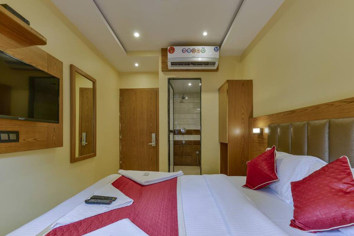 A hotel room with a bed, a TV, a mirror, and an air conditioning unit.