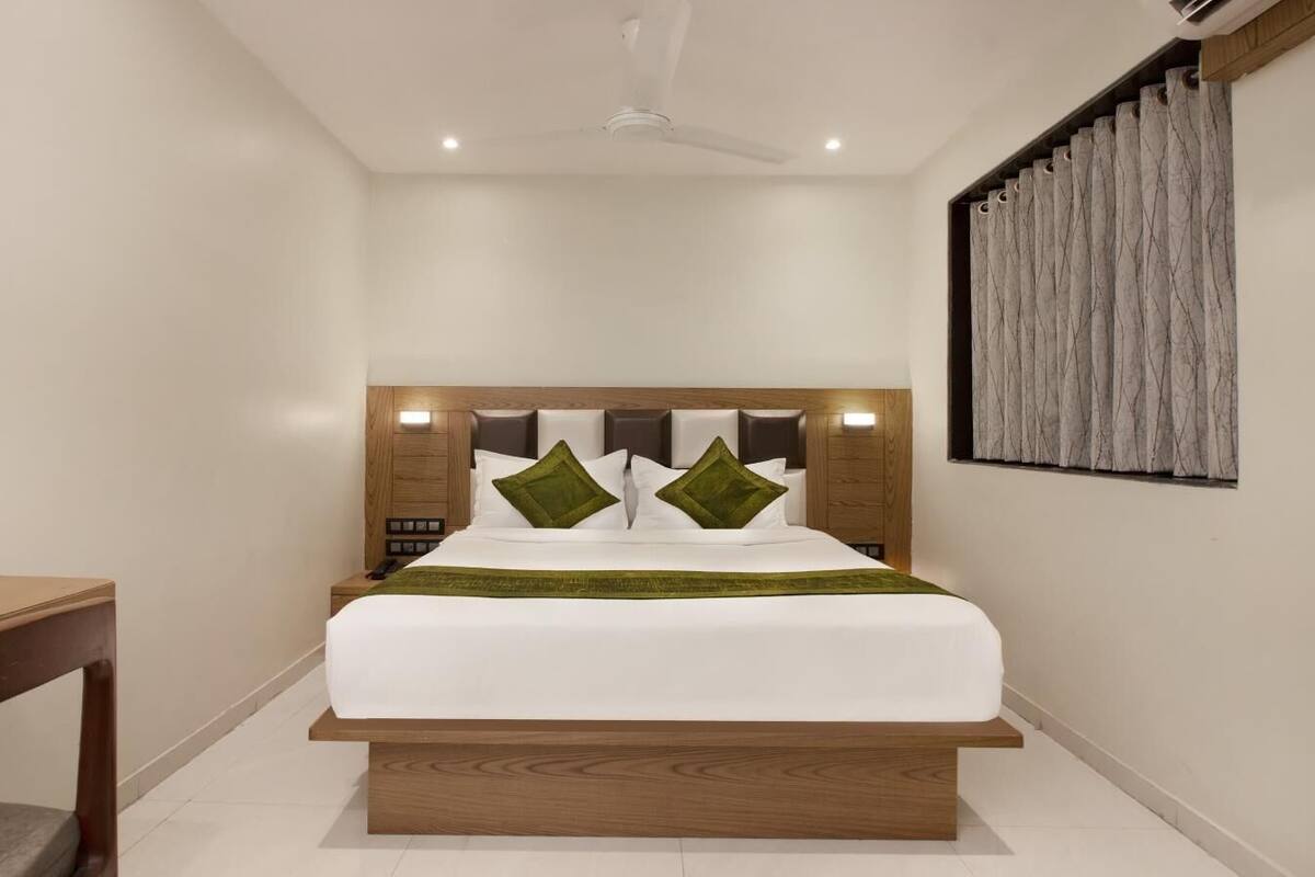A modern bedroom with a wooden headboard, a bed with white bedding and green pillows, a bedside table, and a ceiling fan.