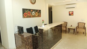 A reception area with a marble counter, black chairs, a clock, and a floral painting. - Treehouse Neo Casa-Unit of Neo Residency (Gurugram)