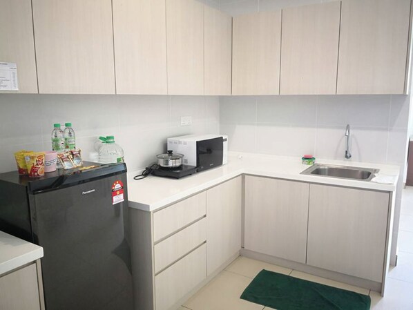 Una cocina compacta con refrigerador, microondas, lavamanos y una pequeña encimera.