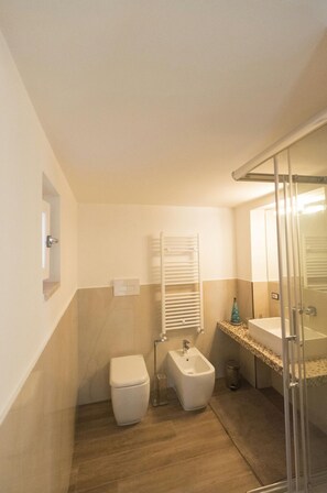 Un baño moderno con inodoro, bidé y zona de ducha con mampara de vidrio.