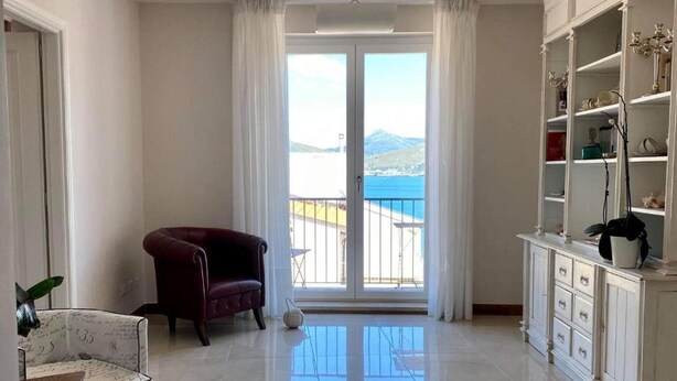 A spacious living room with a large window, a red sofa, a white armchair, and a white cabinet with shelves. - Santa Lucia B&B (Gaeta)